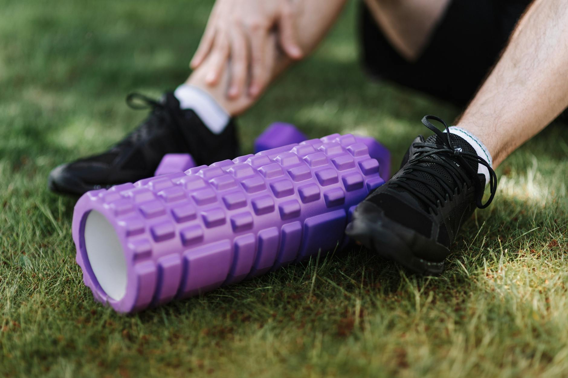 Czarne buty sportowe i fioletowy wałek fitness na trawie