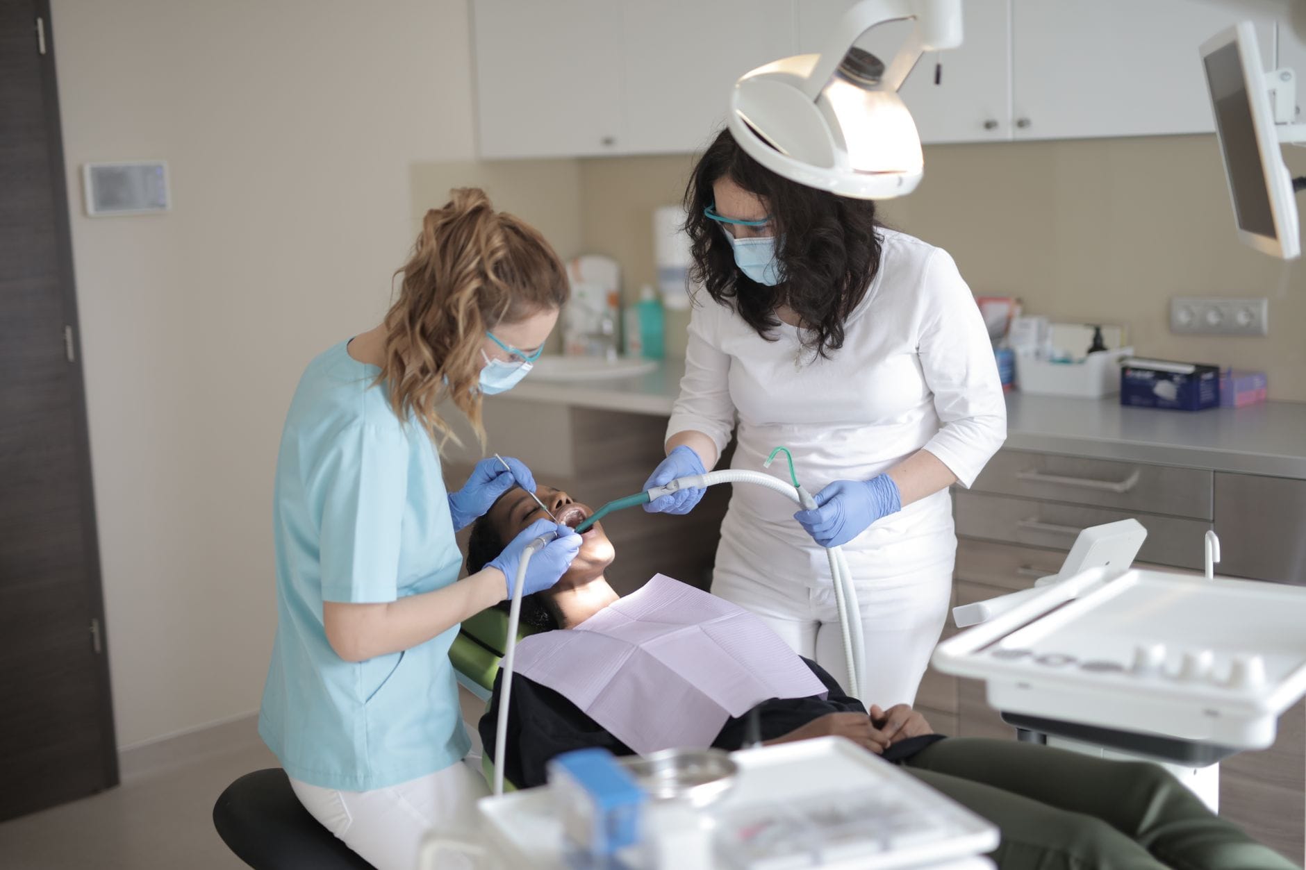 Dentystki w maskach leczą zęby pacjentce w nowoczesnym gabinecie
