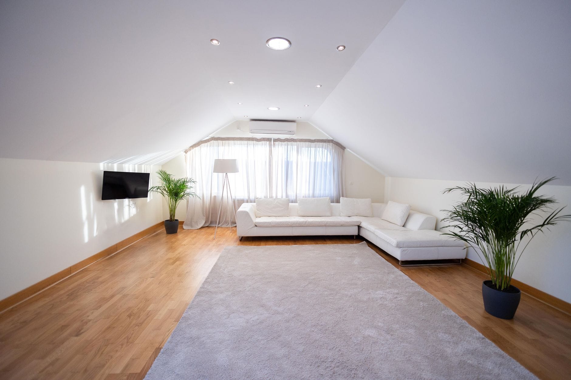 Jasny salon na poddaszu z białą sofą i drewnianą podłogą laminate